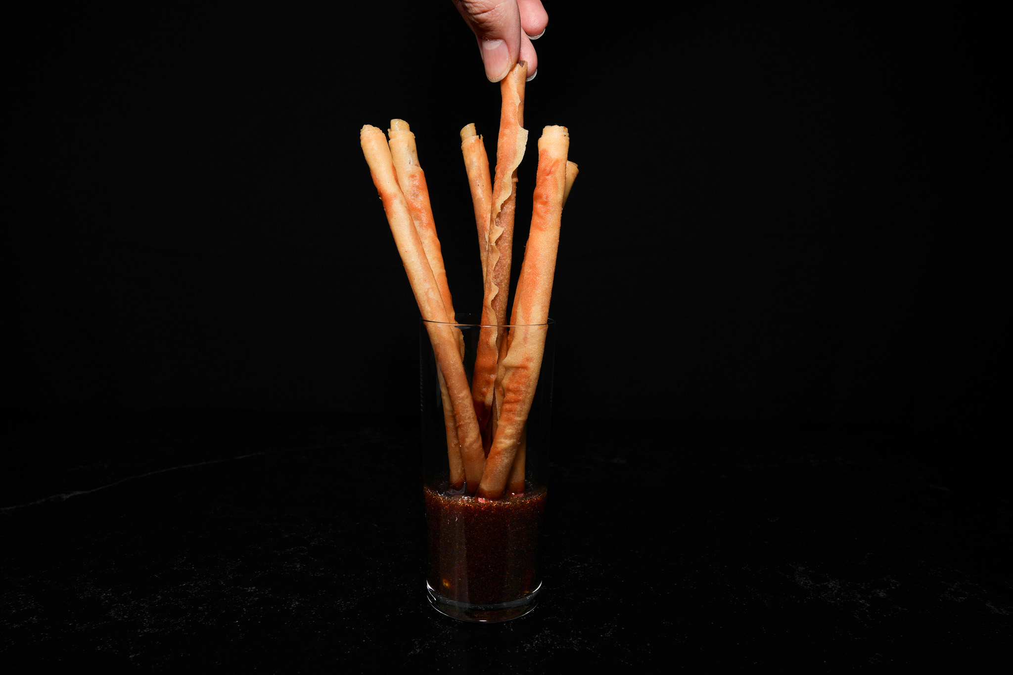 A hand dipping a long breadstick into red sauce