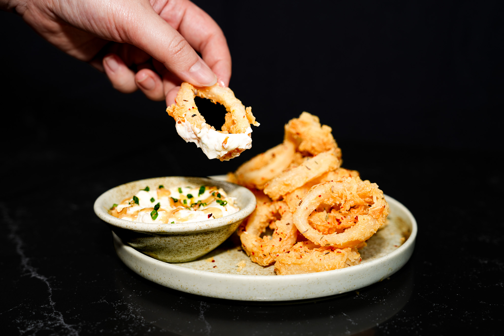 A hand dipping a crisp calamari ring into sauce