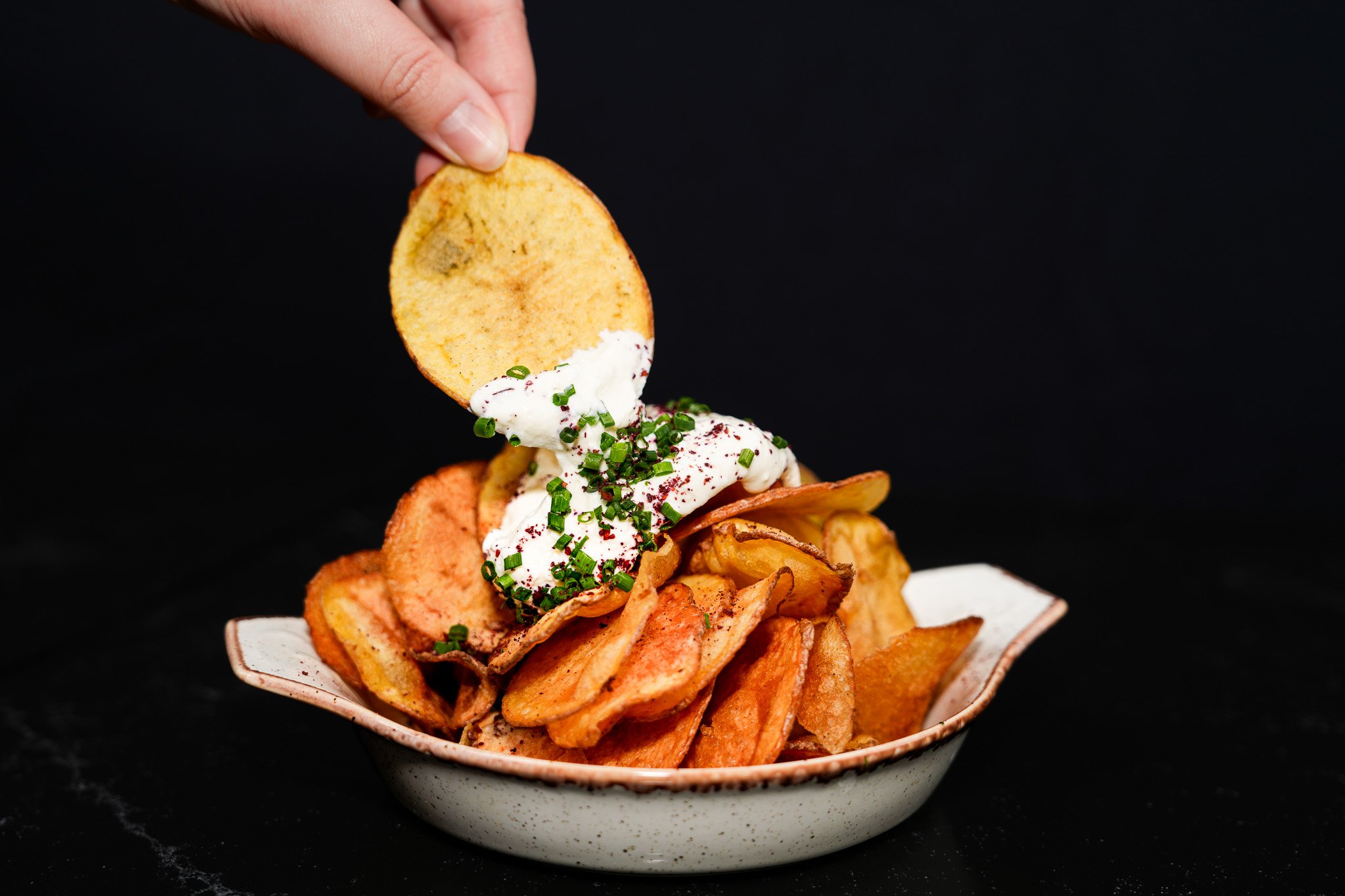 A hand lifting a crisp with herb-topped yogurt dip