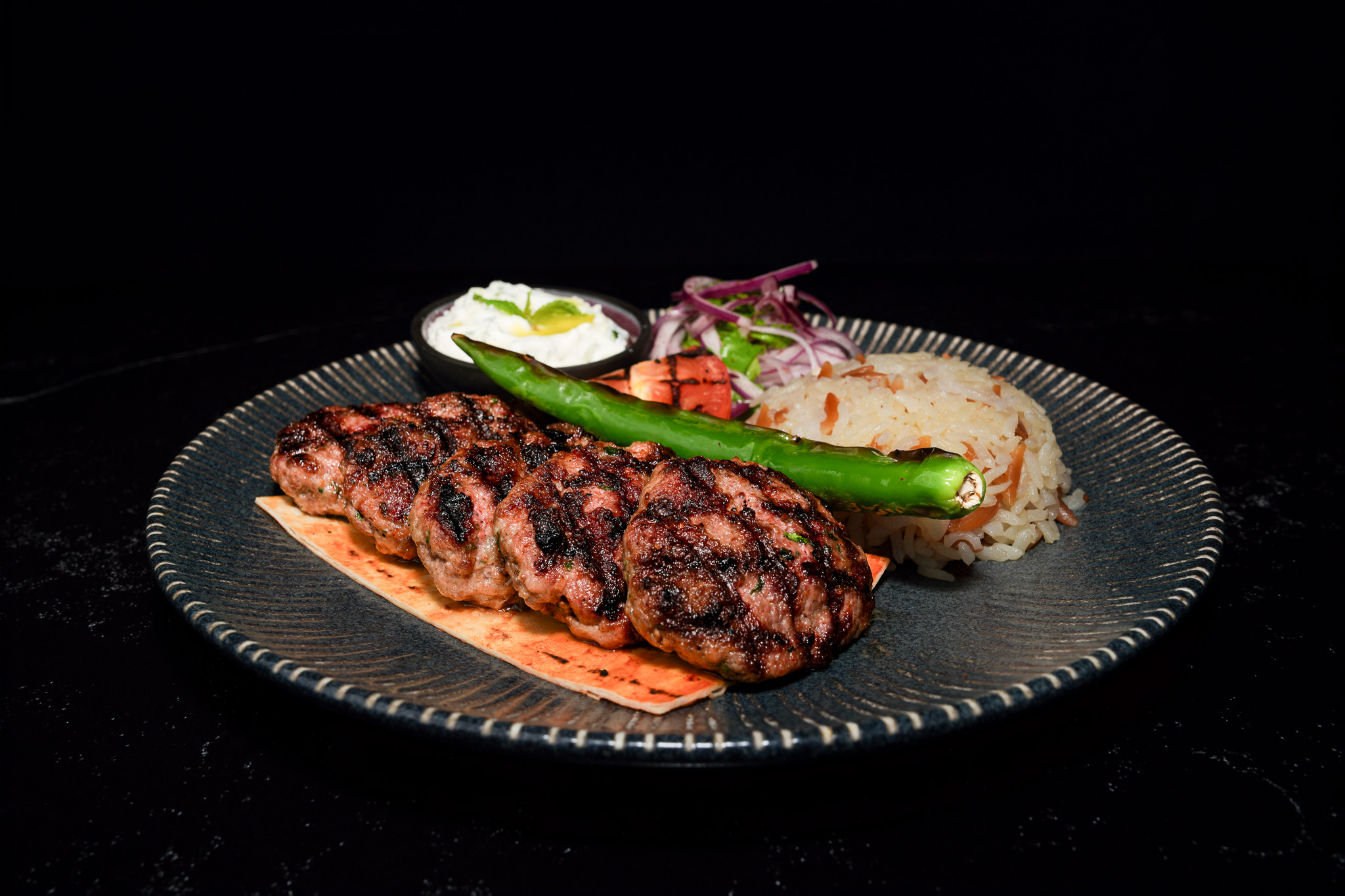 Grilled meat patties served with rice, yogurt, and green pepper