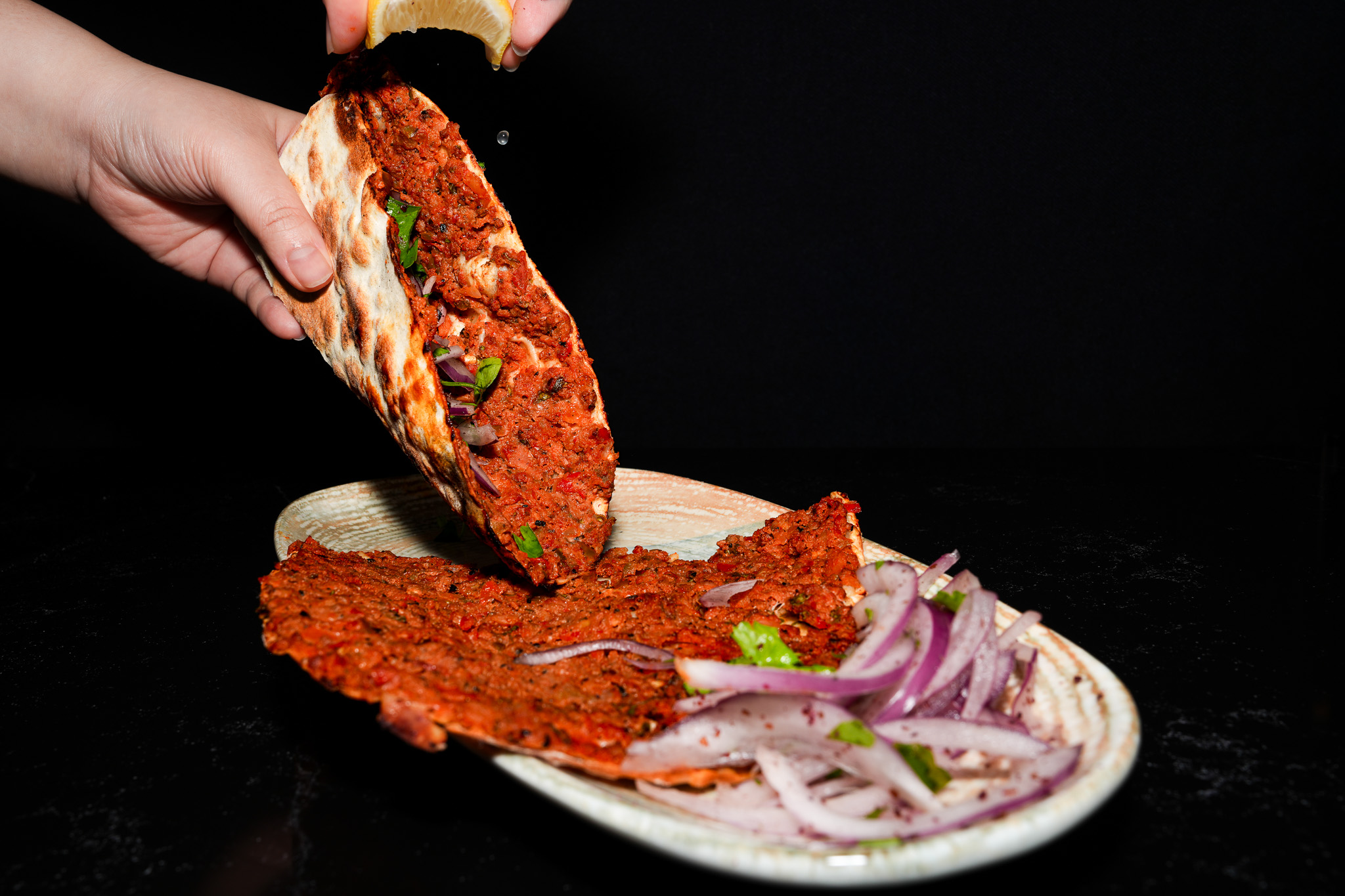 Lemon being squeezed over a folded piece of lahmacun