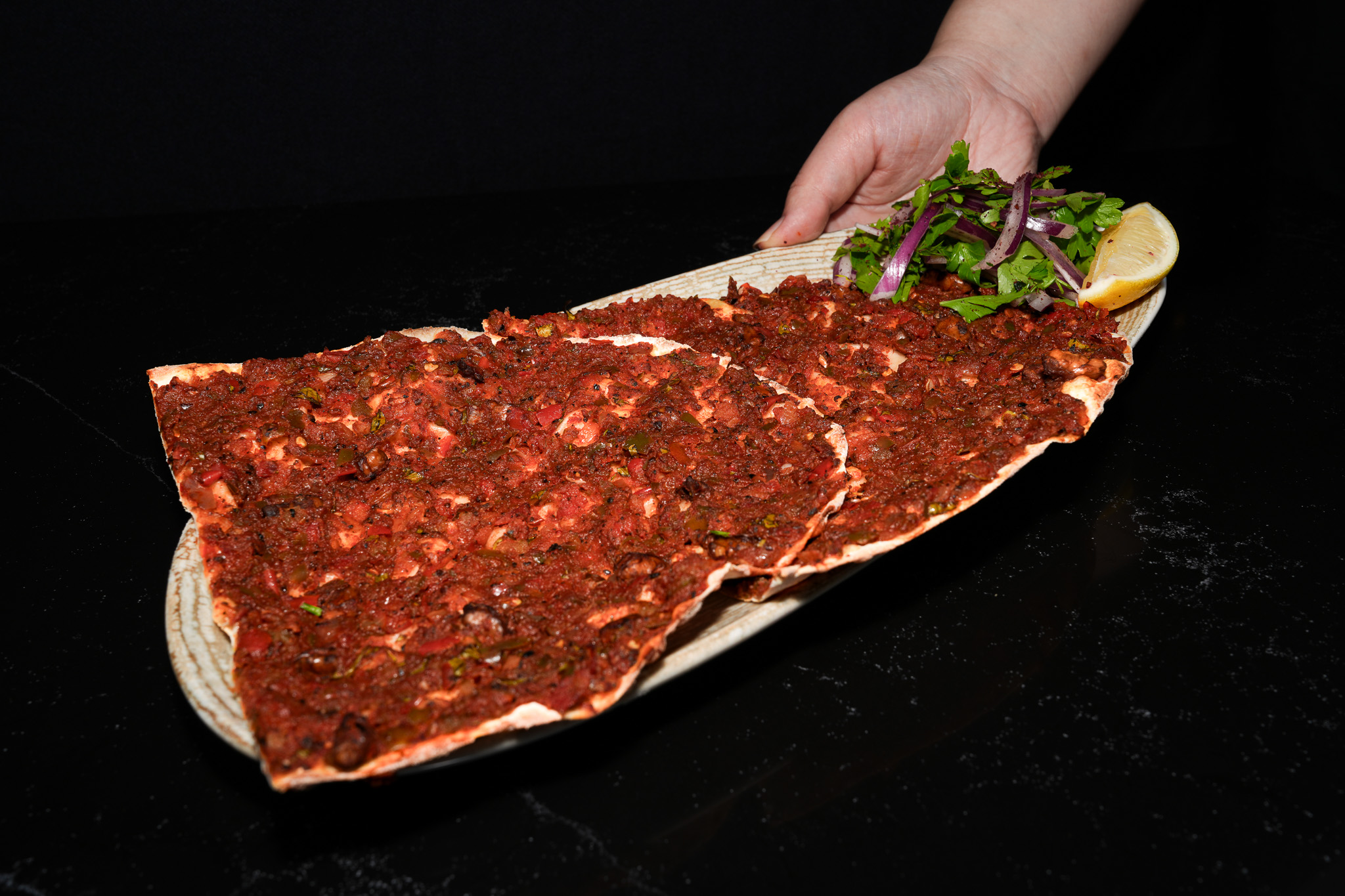 A hand presenting a large lahmacun with onion salad