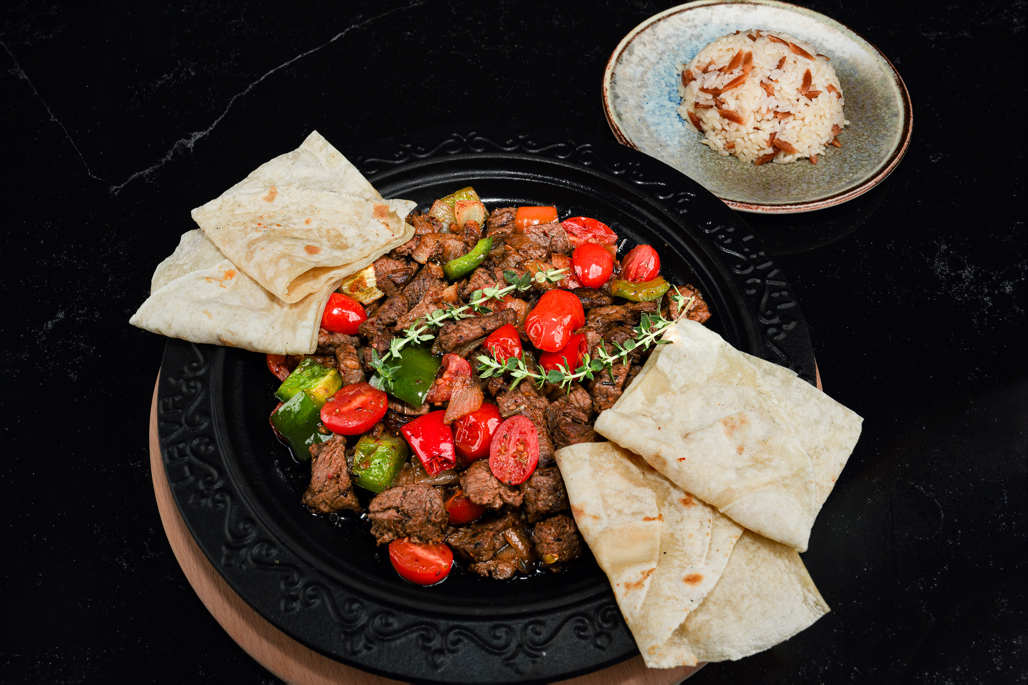 Meat and peppers in a skillet with flatbread and rice, viewed from above