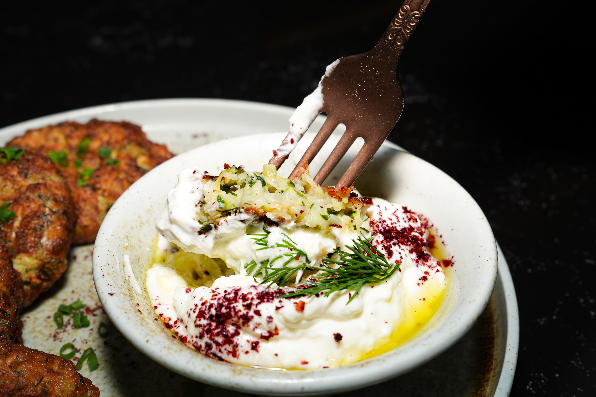 A fork dipping a vegetable fritter into herb-topped yogurt